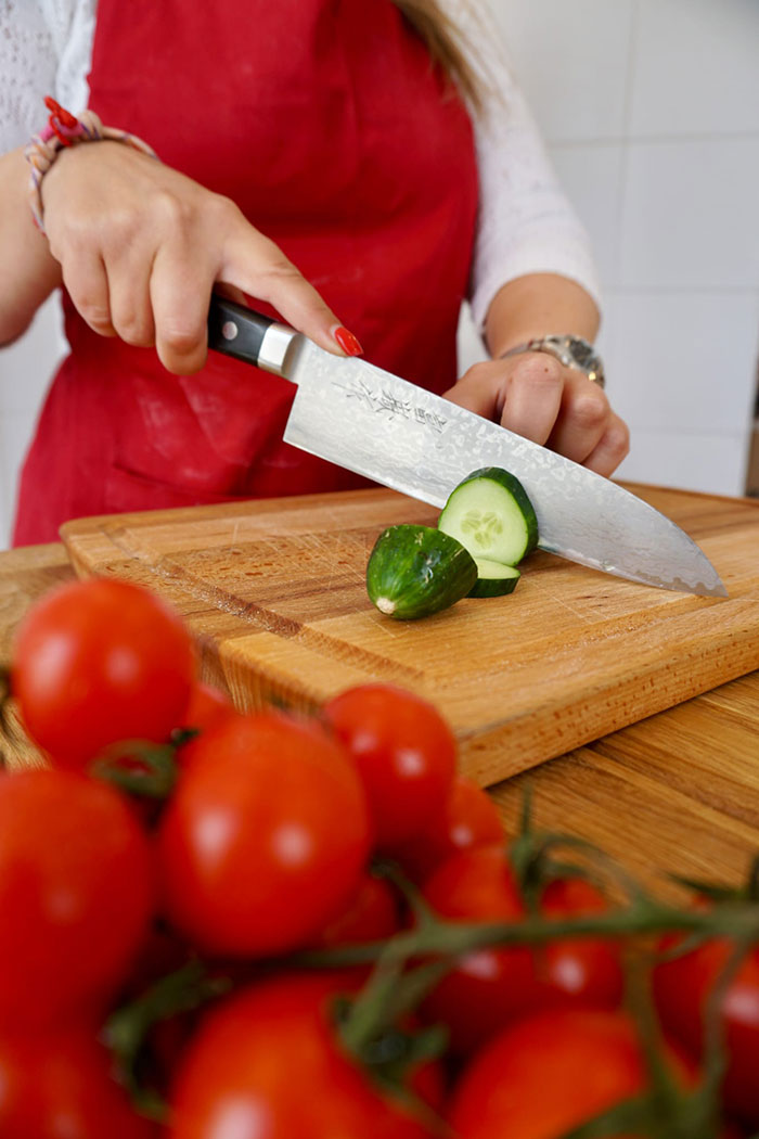 Chef slicing fresh cucumber on a wooden board, with tomatoes in the foreground, showcasing preparation for a gourmet meal by a private chef in Tenerife.