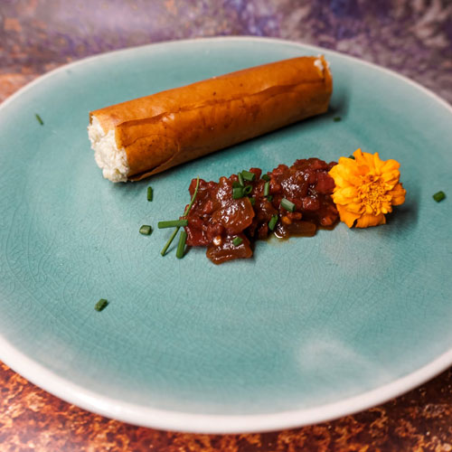 Innovative dessert featuring a cylindrical pastry filled with sweet cream, served with a rich fruit compote and garnished with chives and a marigold flower, created by a private chef in Tenerife.
