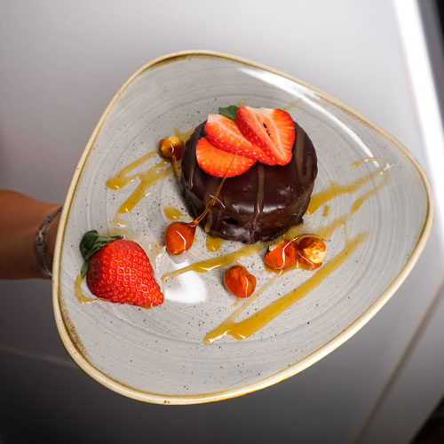 Decadent chocolate dessert topped with fresh strawberries and hazelnuts, drizzled with caramel sauce, elegantly presented by a private chef in Tenerife.