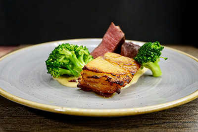 Gourmet plate with seared pork belly, tender beef, broccoli, and creamy sauce, prepared by a private chef in Tenerife.